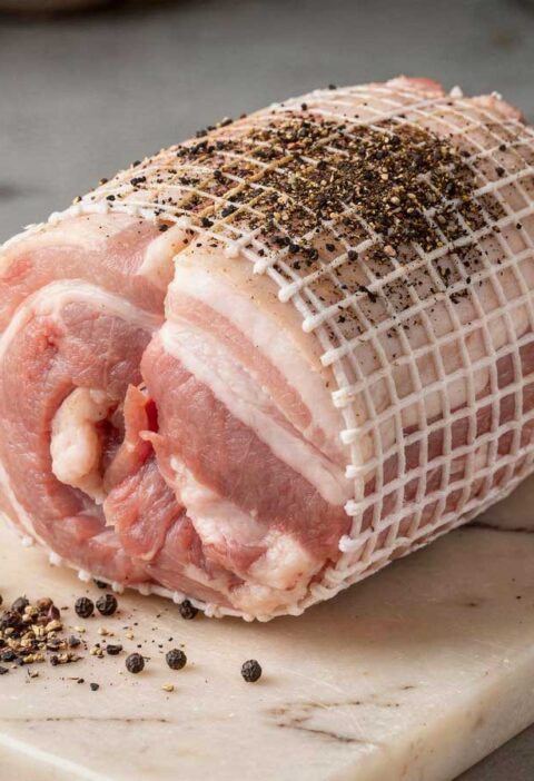 Rauwe spekrollade in een elastisch rolladenet op een marmeren snijplank met peperkorrels