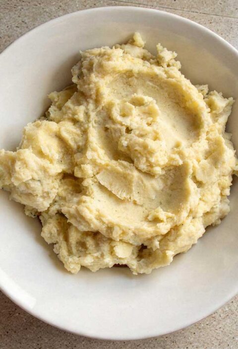 Een gevulde witte schaal met romige, warme aardappelpuree, klaar om geserveerd te worden.