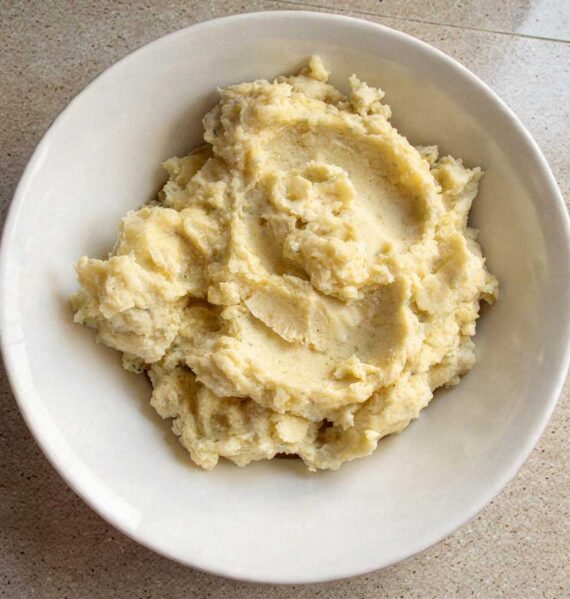 Een gevulde witte schaal met romige, warme aardappelpuree, klaar om geserveerd te worden.