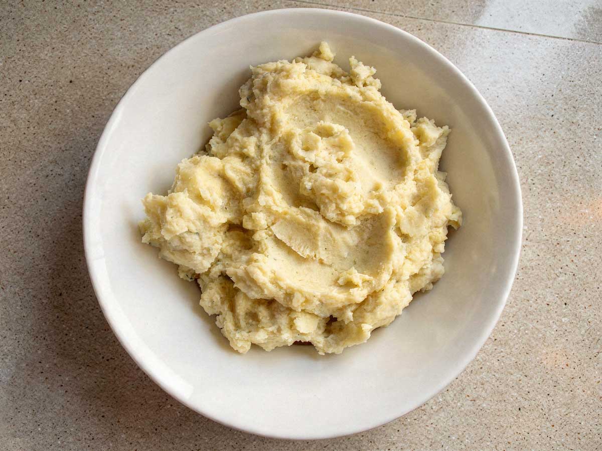 Een gevulde witte schaal met romige, warme aardappelpuree, klaar om geserveerd te worden.