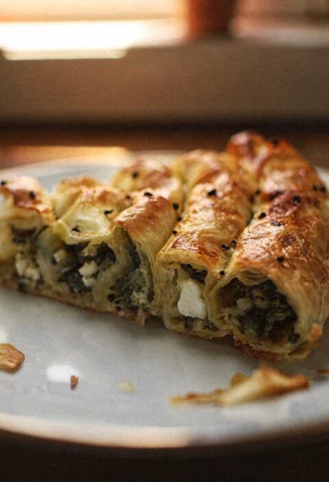 Een stuk goudbruine börek gevuld met spinazie en feta op een wit bord.
