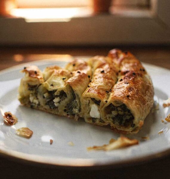 Een stuk goudbruine börek gevuld met spinazie en feta op een wit bord.