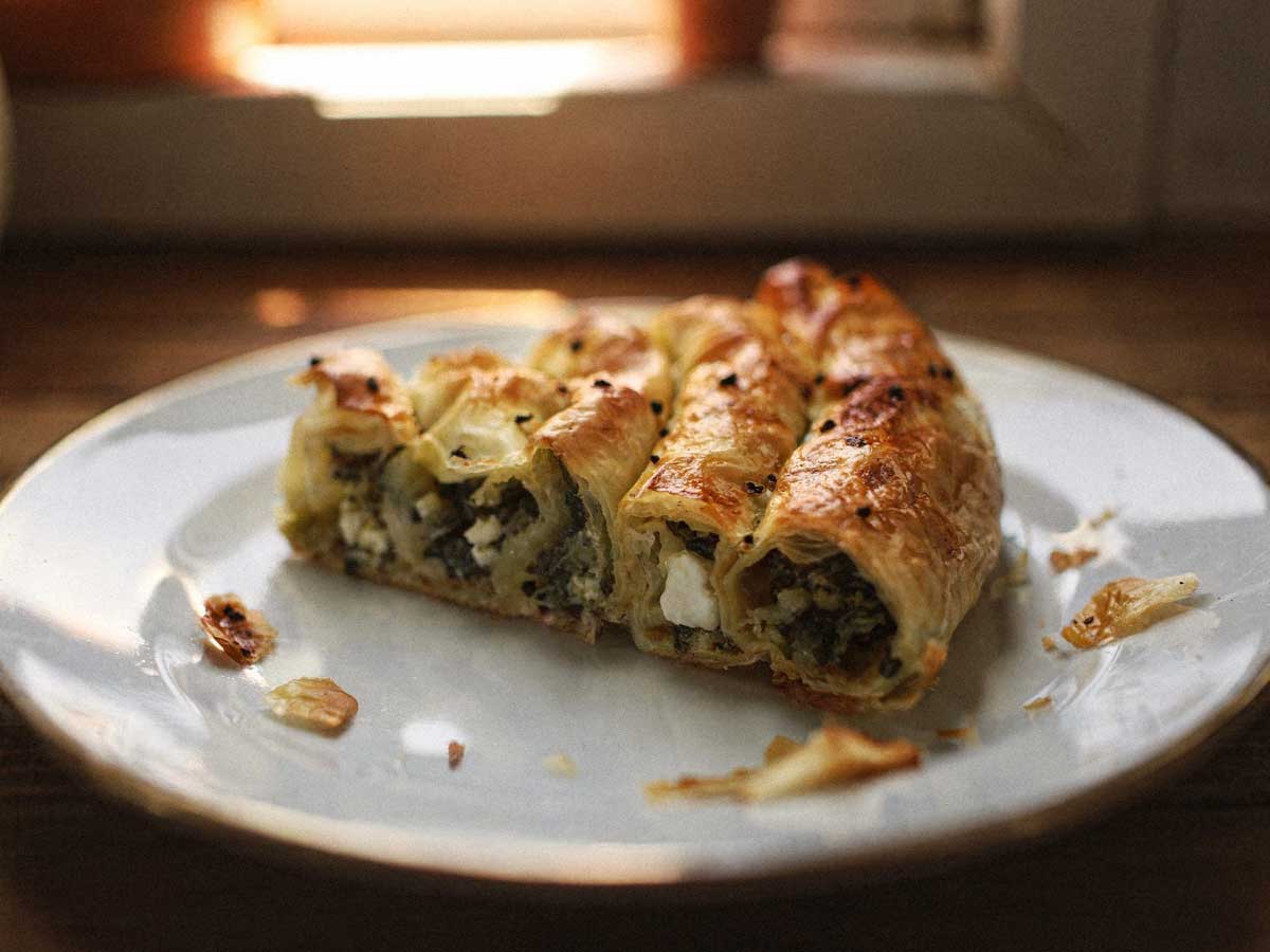 Een stuk goudbruine börek gevuld met spinazie en feta op een wit bord.