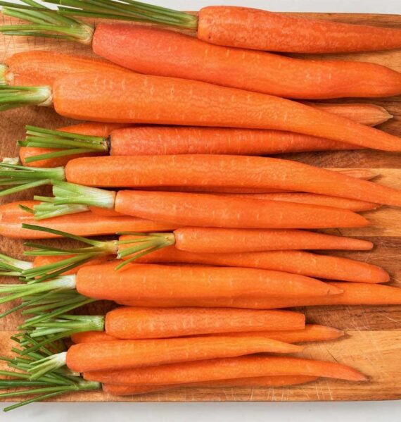 Een houten snijplank vol met schoongemaakte, feloranje bospeen klaar om te koken.