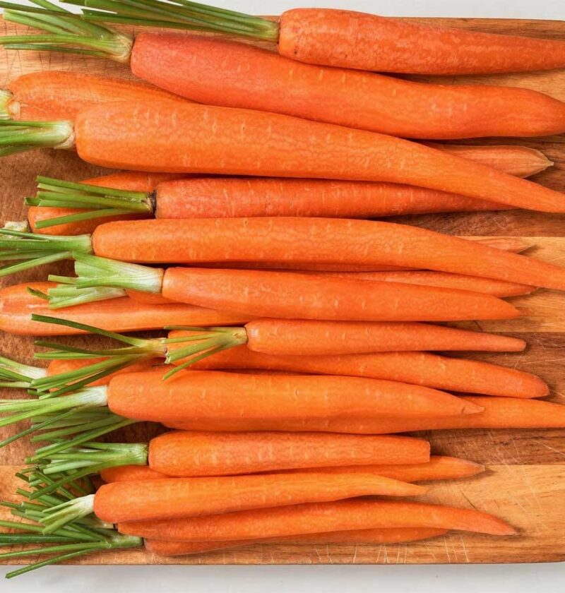 Een houten snijplank vol met schoongemaakte, feloranje bospeen klaar om te koken.