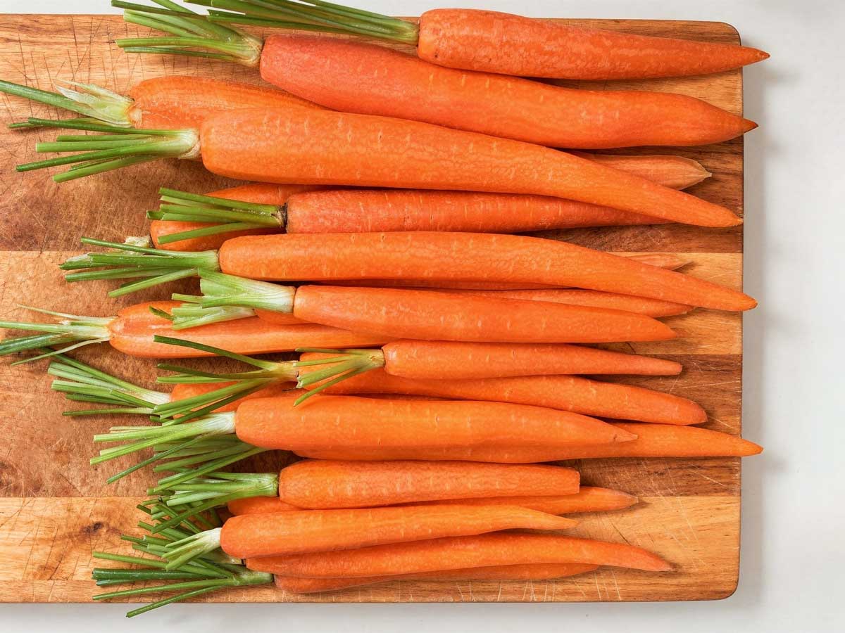 Een houten snijplank vol met schoongemaakte, feloranje bospeen klaar om te koken.