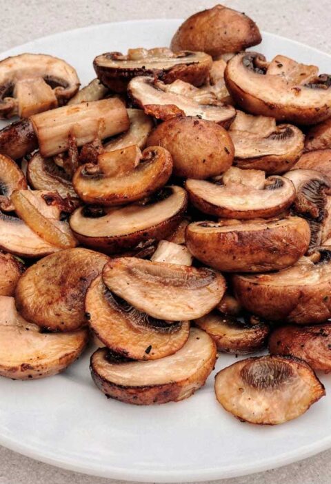 Een portie goudbruin gebakken plakjes champignons op een wit bord.