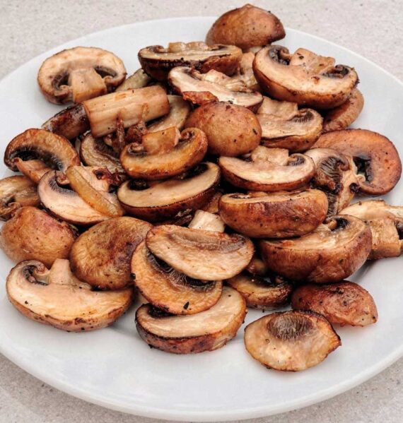 Een portie goudbruin gebakken plakjes champignons op een wit bord.