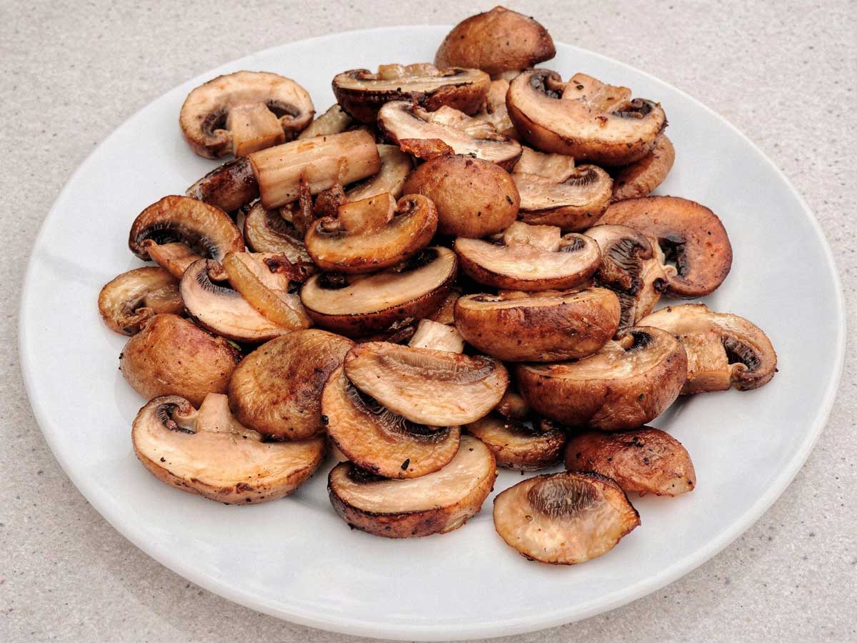 Een portie goudbruin gebakken plakjes champignons op een wit bord.