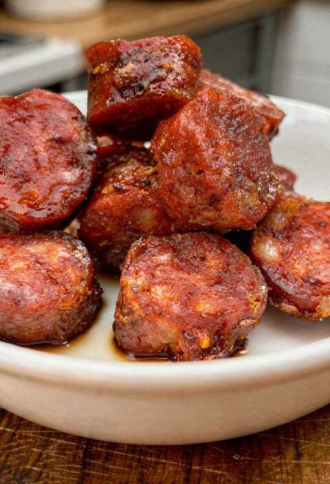 Dikke plakken gebakken chorizo met een krokant randje in een wit schaaltje.