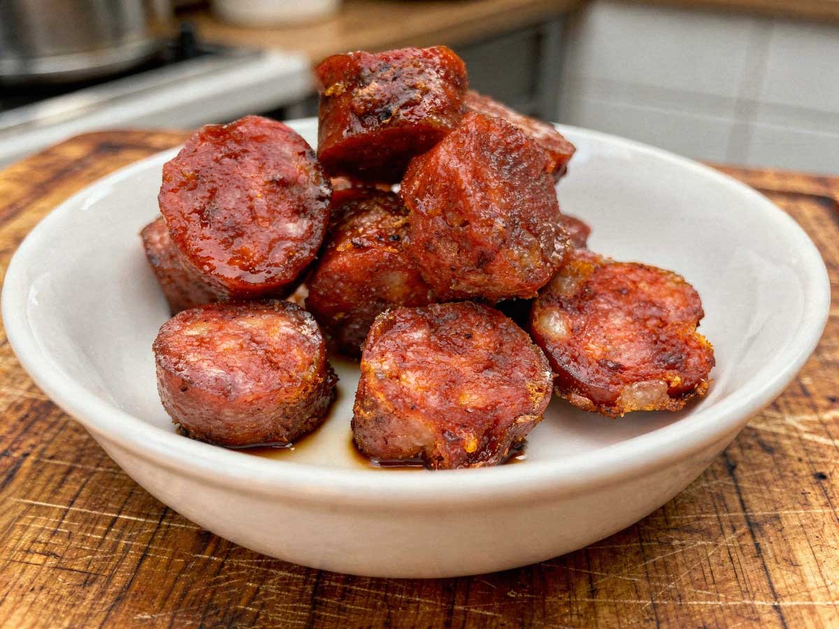 Dikke plakken gebakken chorizo met een krokant randje in een wit schaaltje.