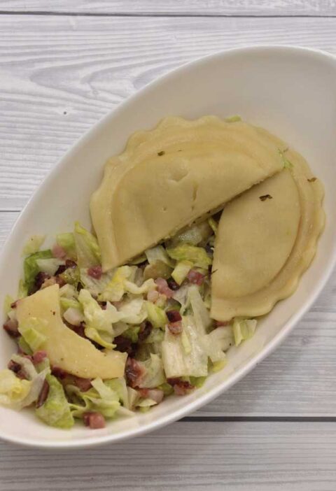 Een heerlijke groene salade met appel, spek en verse ravioli, in een wit schaaltje.
