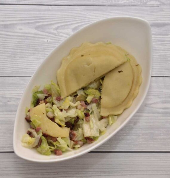 Een heerlijke groene salade met appel, spek en verse ravioli, in een wit schaaltje.