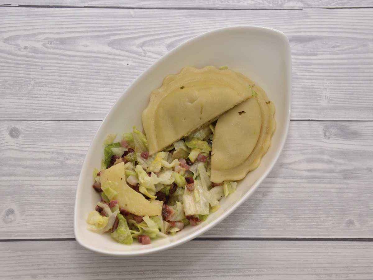 Een heerlijke groene salade met appel, spek en verse ravioli, in een wit schaaltje.