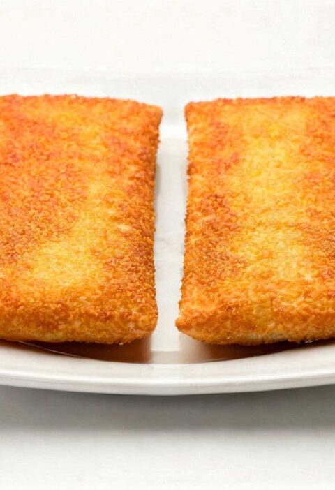 Twee goudbruin gebakken kaassoufflés op een vierkant wit bord onder helder studiolicht.
