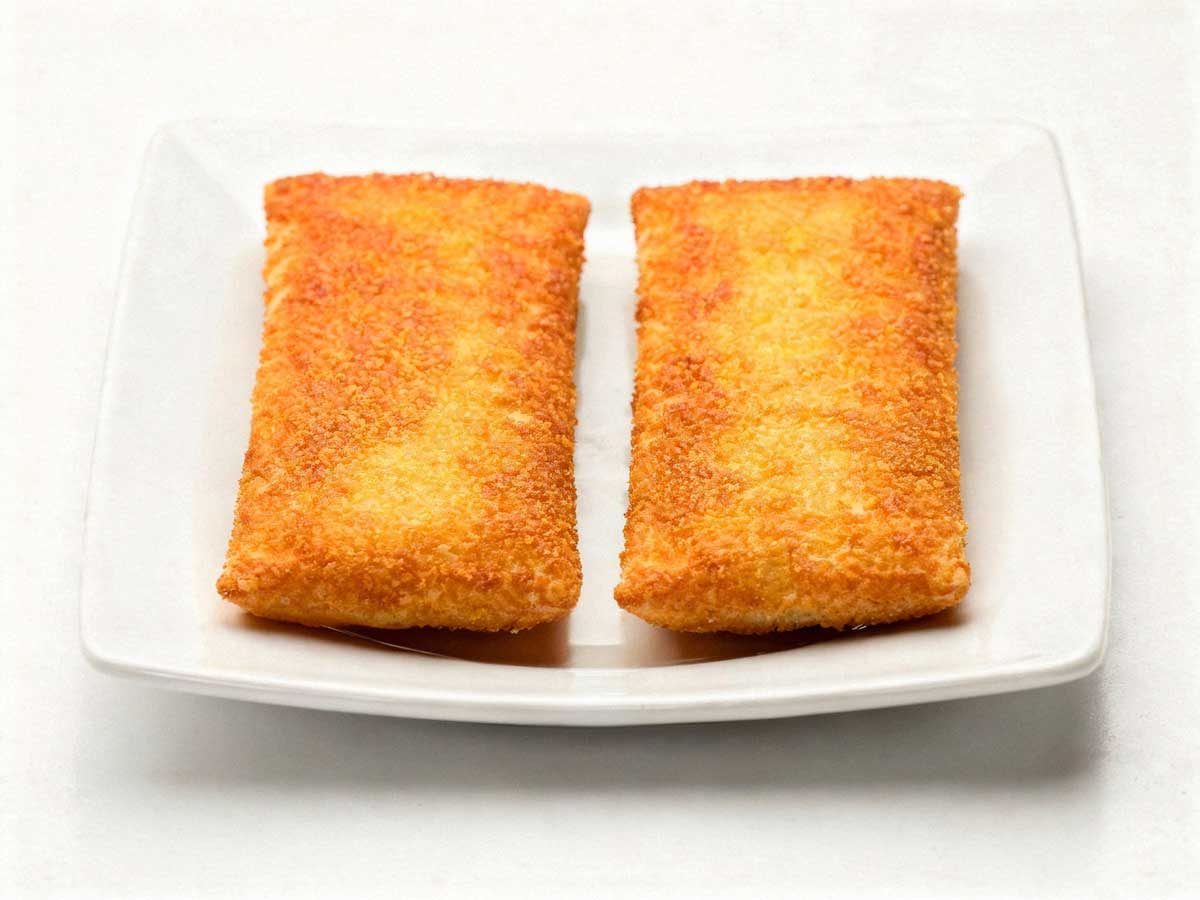 Twee goudbruin gebakken kaassoufflés op een vierkant wit bord onder helder studiolicht.