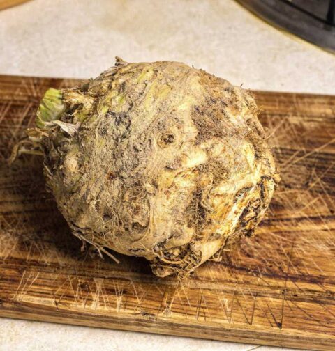 Een grote, ongeschilde verse knolselderij op een houten snijplank in de keuken.