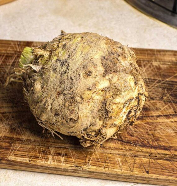 Een grote, ongeschilde verse knolselderij op een houten snijplank in de keuken.