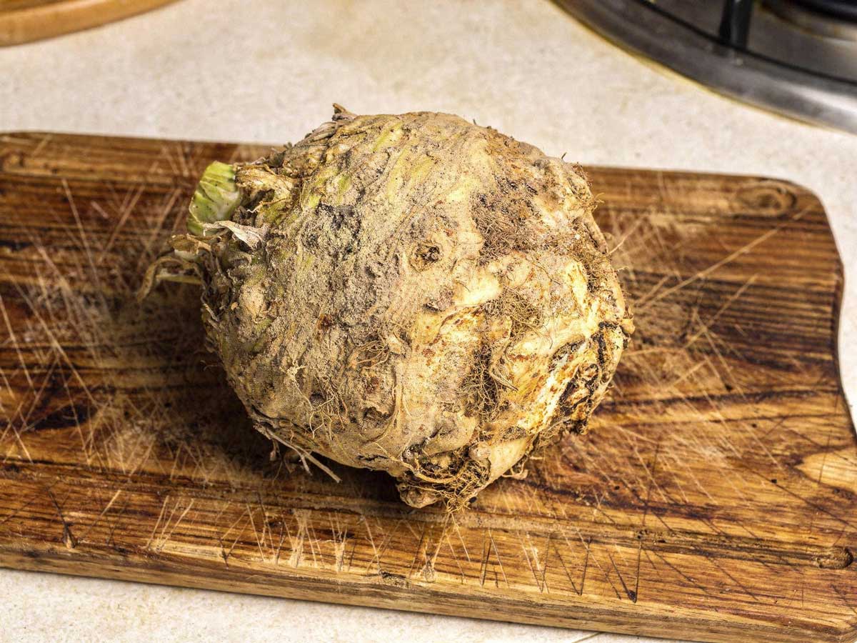 Een grote, ongeschilde verse knolselderij op een houten snijplank in de keuken.