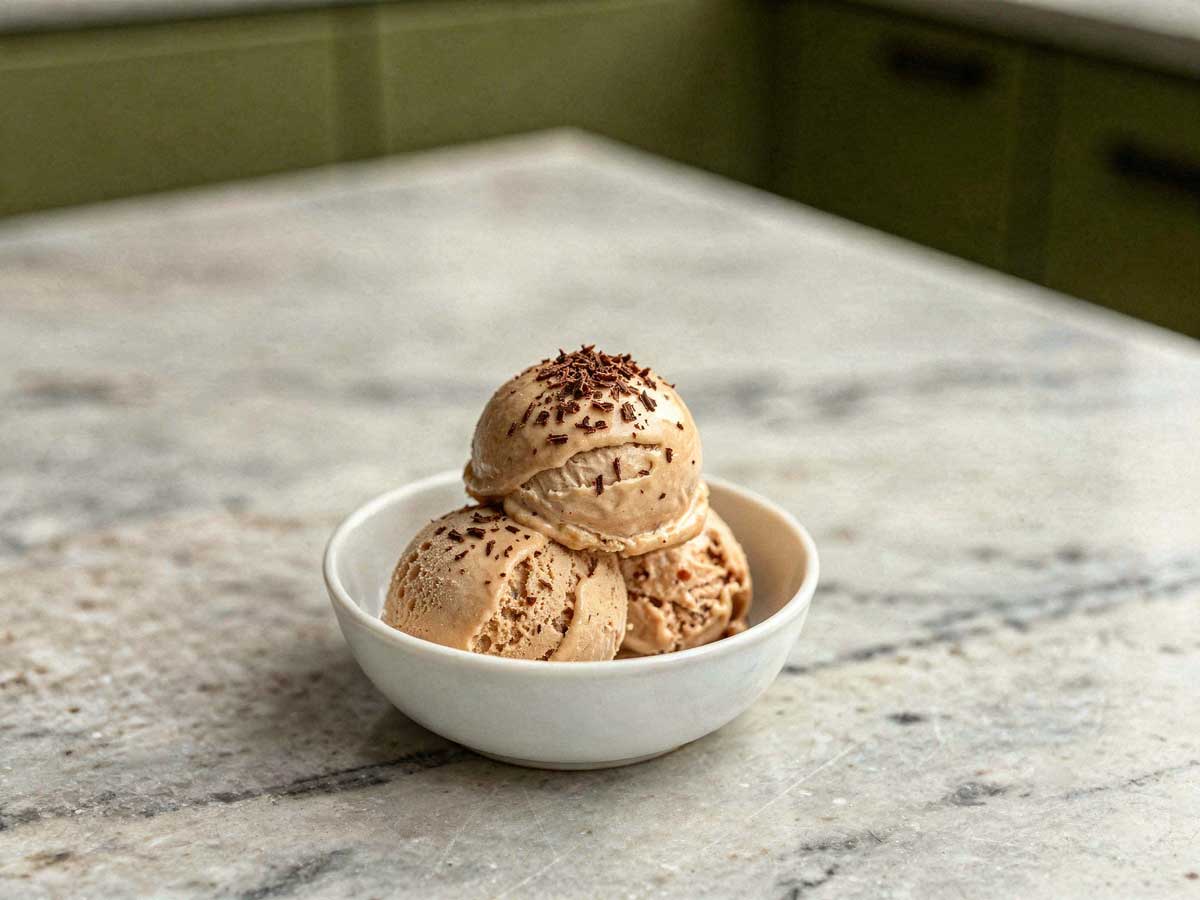 Drie bollen ambachtelijk koffie roomijs met chocoladeschaafsel in een wit schaaltje.