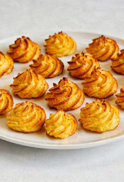 Een lage, brede witte schaal met een laag goudbruin gefrituurde pommes duchesse rosetten