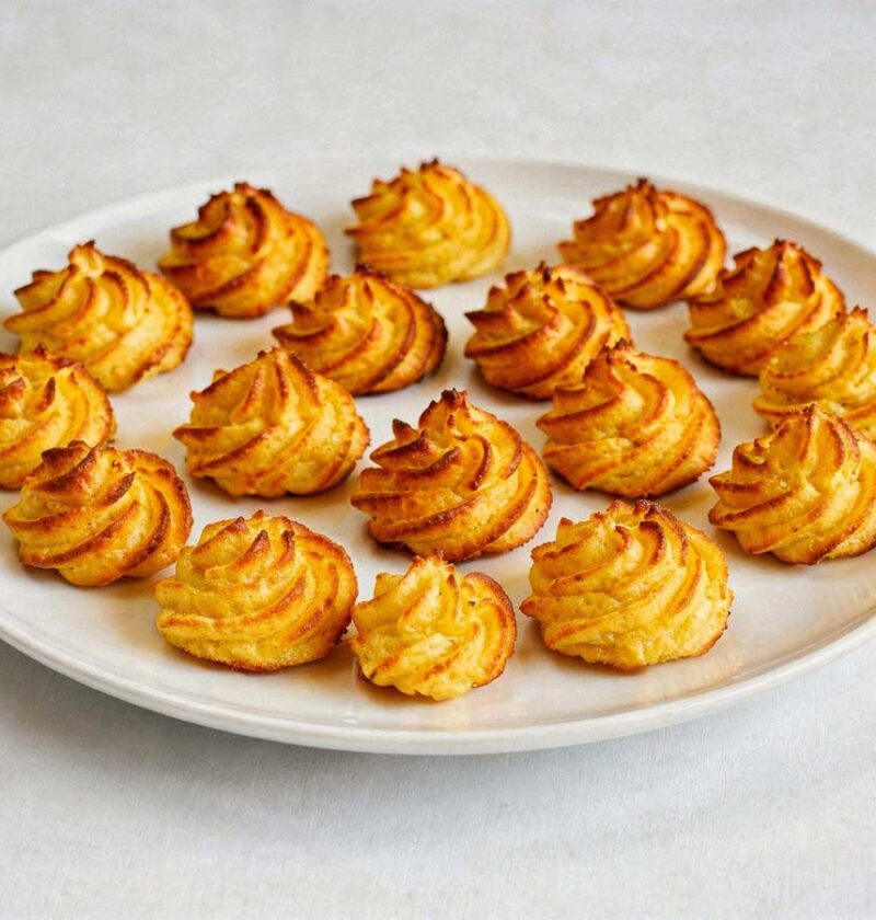 Een lage, brede witte schaal met een laag goudbruin gefrituurde pommes duchesse rosetten