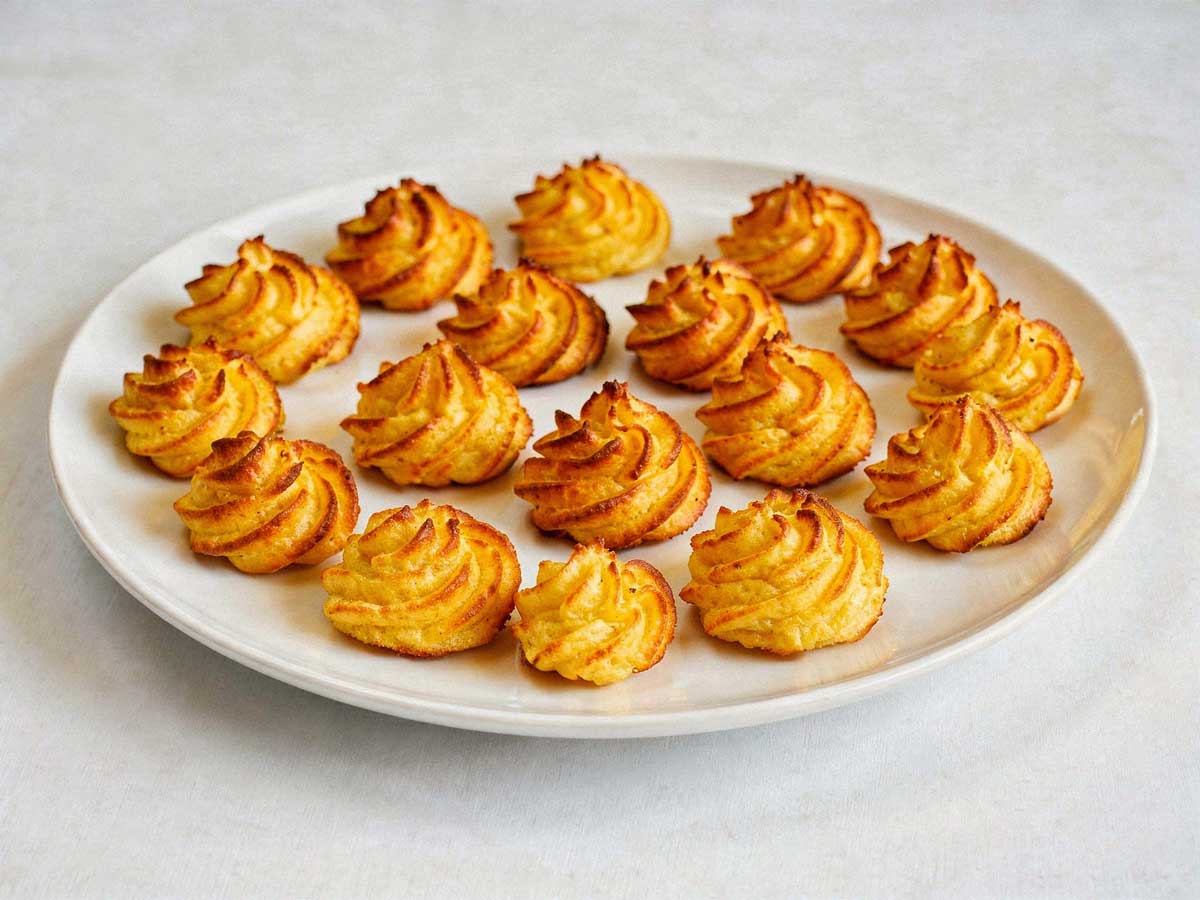 Een lage, brede witte schaal met een laag goudbruin gefrituurde pommes duchesse rosetten