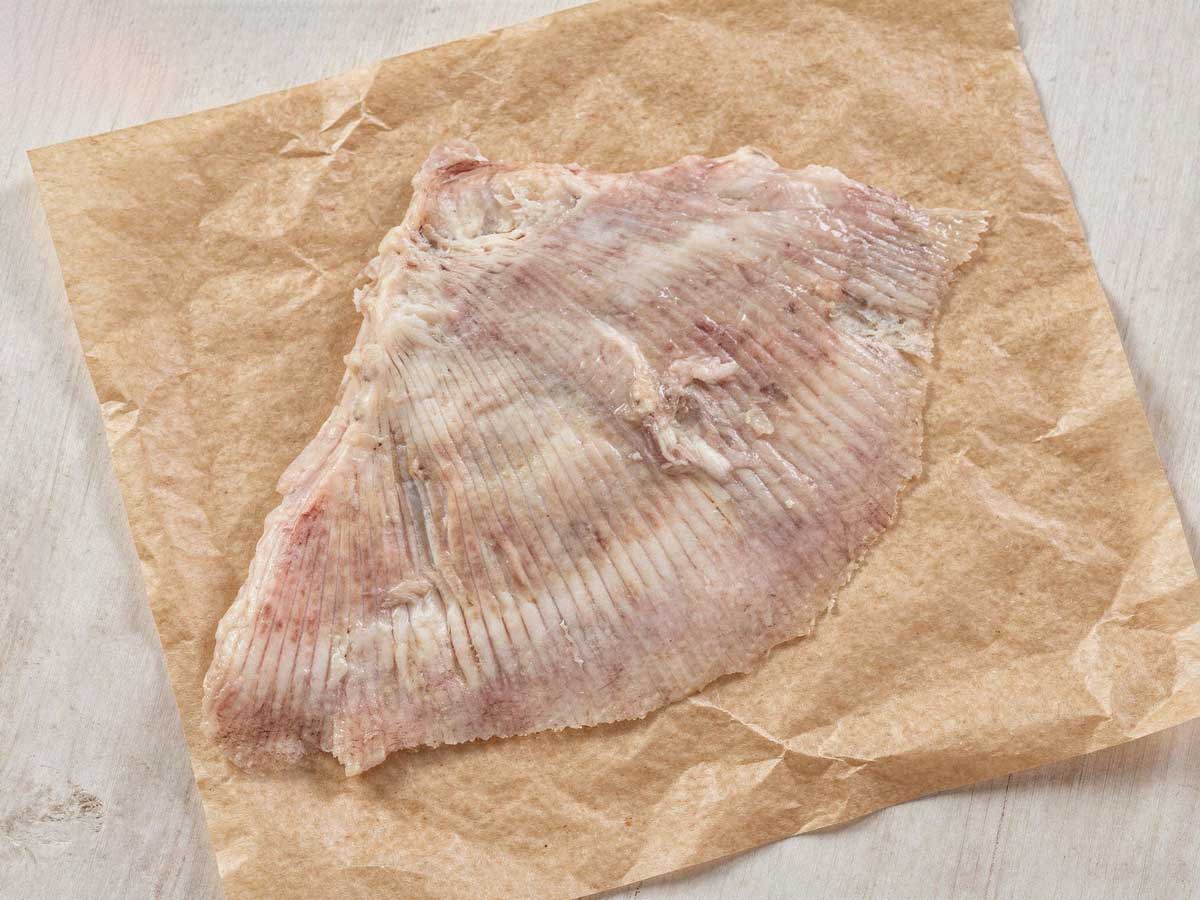 Verse rauwe rogvleugel op een vierkant stuk slagerspapier, klaar om te bakken.