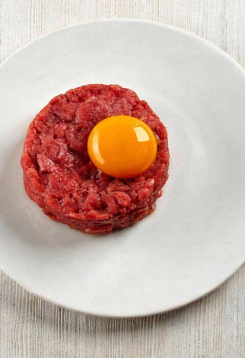 Klassieke steak tartaar elegant opgemaakt op een klein wit bordje.