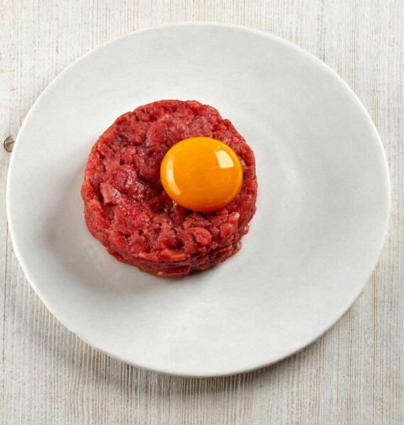 Klassieke steak tartaar elegant opgemaakt op een klein wit bordje.