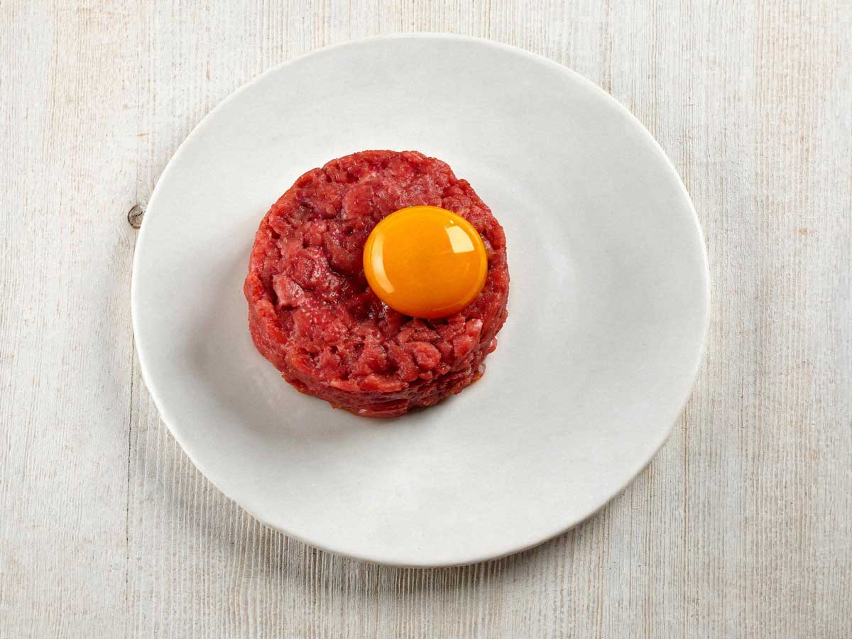 Klassieke steak tartaar elegant opgemaakt op een klein wit bordje.