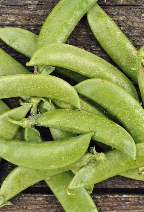 Verse, felgroene sugar snaps verspreid op een rustieke houten tafel met waterdruppels.