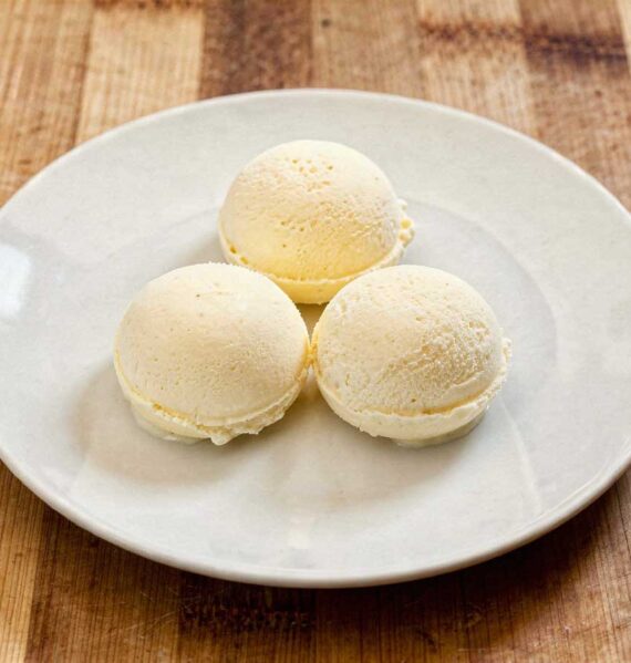 Drie perfect ronde bollen romig vanille-ijs geserveerd op een wit bord op een rustieke houten tafel.