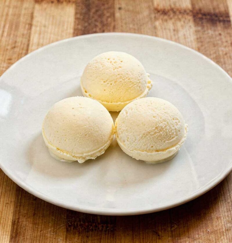 Drie perfect ronde bollen romig vanille-ijs geserveerd op een wit bord op een rustieke houten tafel.