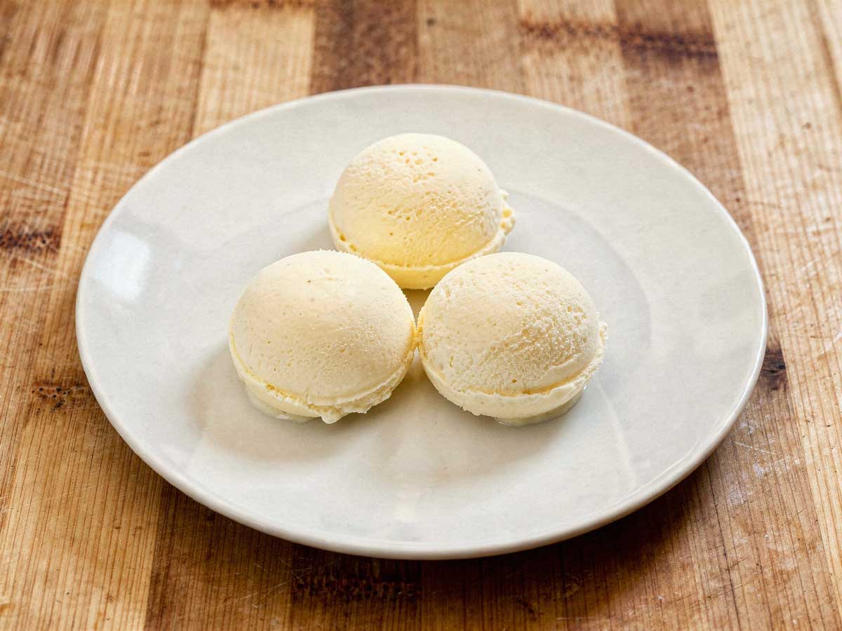 Drie perfect ronde bollen romig vanille-ijs geserveerd op een wit bord op een rustieke houten tafel.