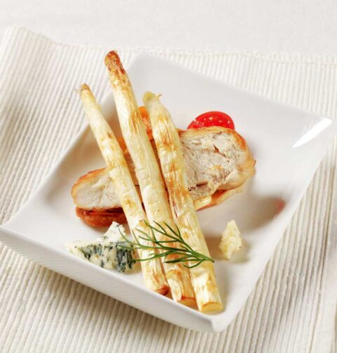 3 gebakken witte asperges op een bord met onder andere een stuk gebakken kip.