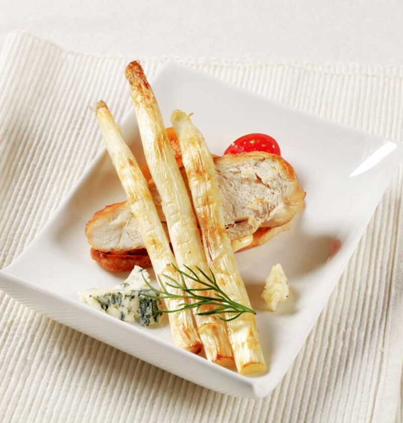3 gebakken witte asperges op een bord met onder andere een stuk gebakken kip.