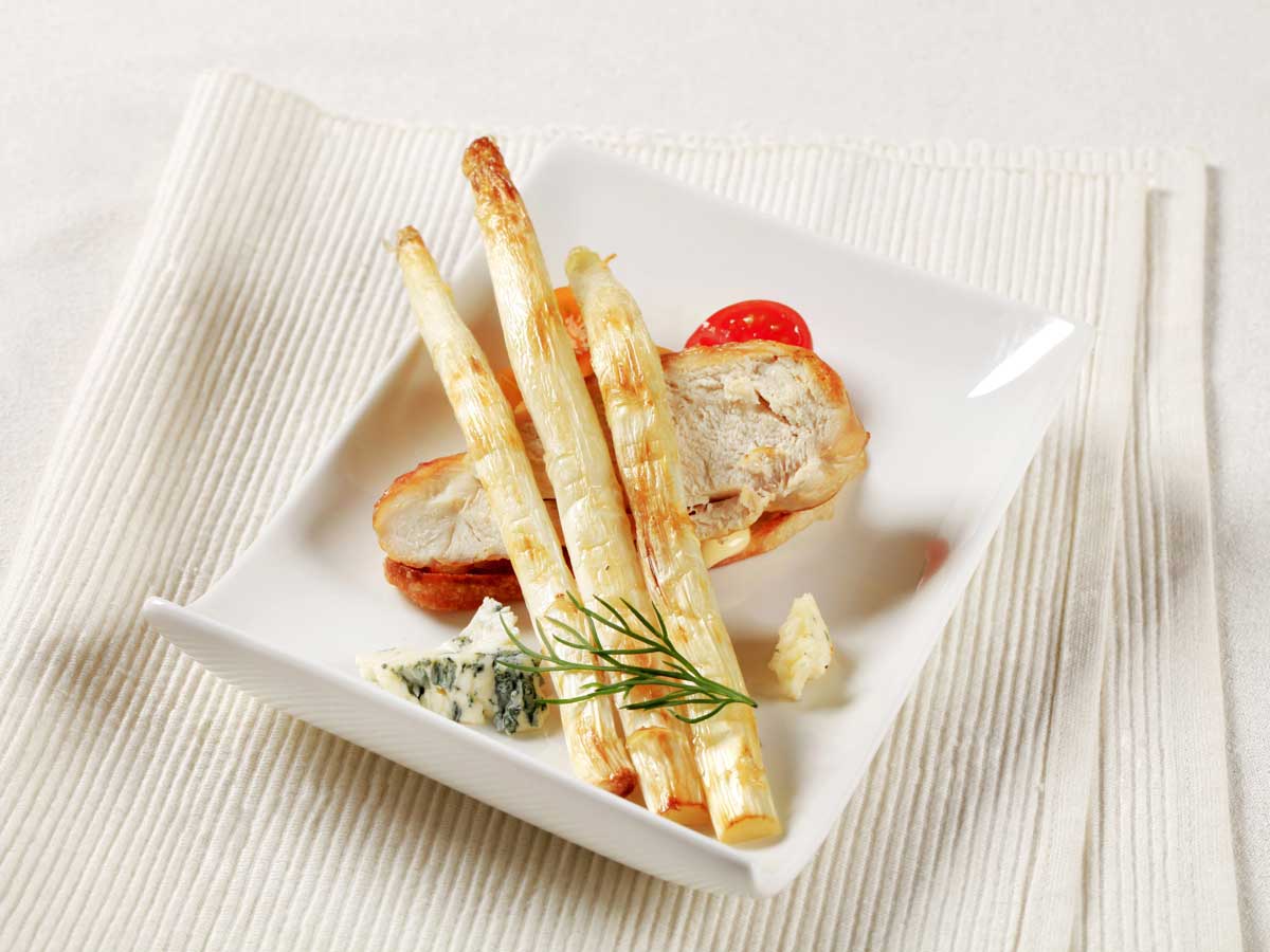 3 gebakken witte asperges op een bord met onder andere een stuk gebakken kip.