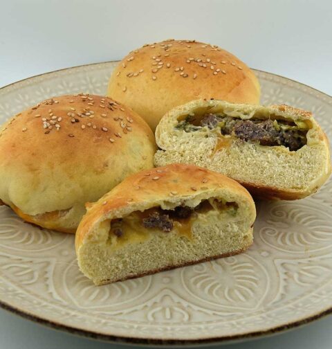 3 Cheeseburgers in een broodje, waarvan er 1 doormidden is gesneden zodat je de cheeseburger in het broodje kunt zien.