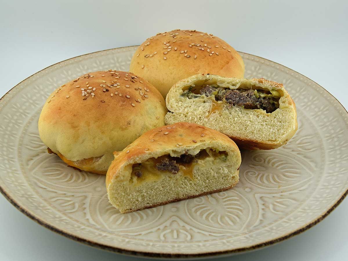3 Cheeseburgers in een broodje, waarvan er 1 doormidden is gesneden zodat je de cheeseburger in het broodje kunt zien.