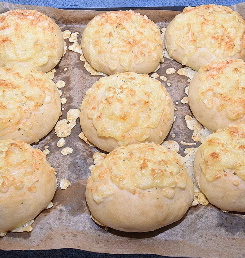 Negen kaasbroodjes liggen op een bakplaat om af te koelen.