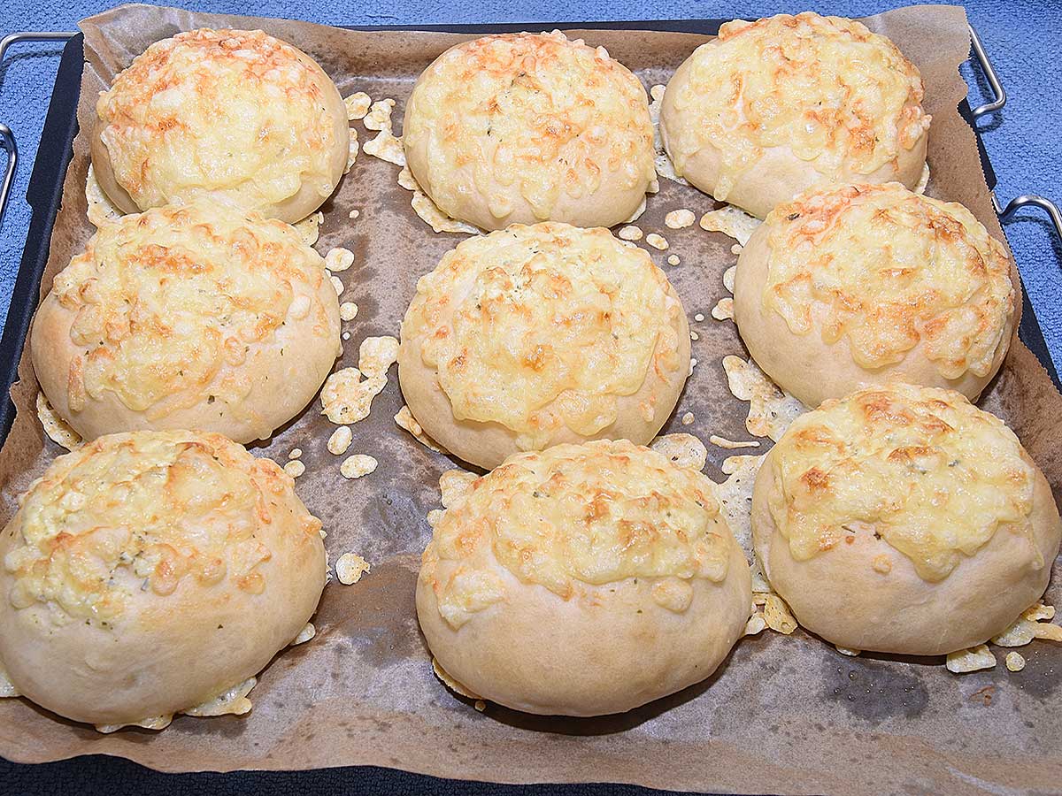 Negen kaasbroodjes liggen op een bakplaat om af te koelen.