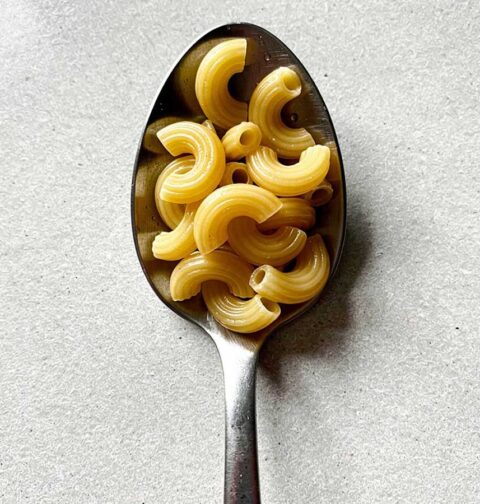 Een eetlepel met ongekookte macaroni, om aan te geven hoeveel een eetlepel eigenlijk is.