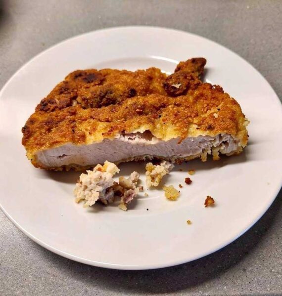 Een doormidden gesneden schnitzel waaraan je goed kan zien dat de paneerlaag eigenlijk te dik en te nat is.