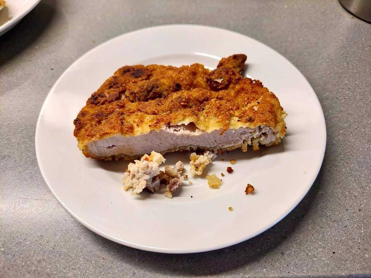 Een doormidden gesneden schnitzel waaraan je goed kan zien dat de paneerlaag eigenlijk te dik en te nat is.