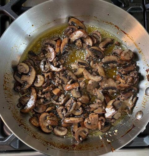 Een koekenpan waarin plakjes champignons worden gesauteerd.