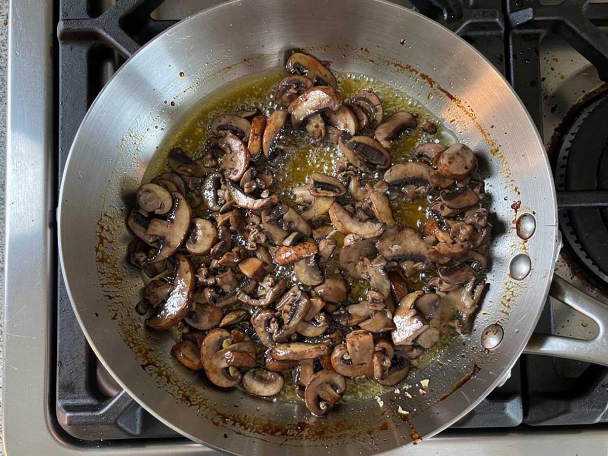 Een koekenpan waarin plakjes champignons worden gesauteerd.