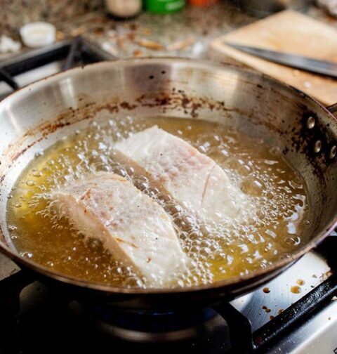 Twee visfilets die net in de koekenpan gelegd zijn om te bakken.