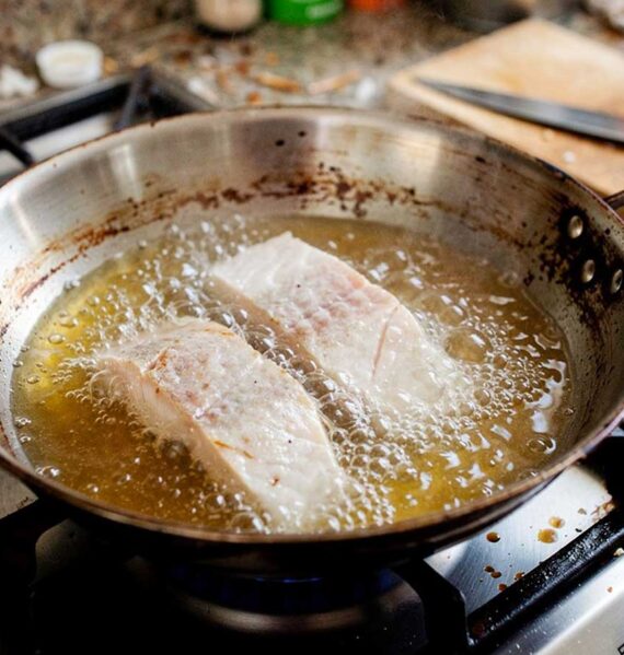 Twee visfilets die net in de koekenpan gelegd zijn om te bakken.