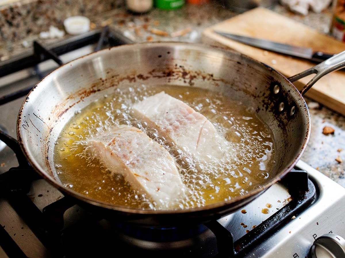 Twee visfilets die net in de koekenpan gelegd zijn om te bakken.